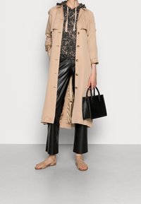 Gabat de color beige sobre una sudadera negra con estampado, combinado con pantalones de cuero negros y sandalias beige. Bolso negro con asas cortas.