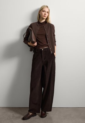 Brown cardigan with buttons, layered over a brown top. Wide-legged corduroy pants with pockets. Brown loafers and a textured clutch.