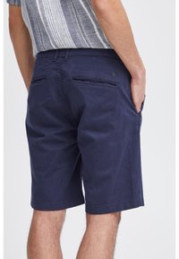 Shorts bleu marine en coton avec un devant plat, des poches arrière et une texture lisse. L'ourlet est légèrement retroussé.