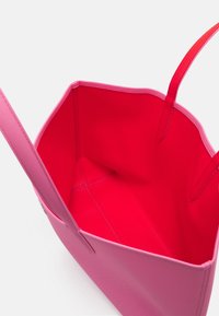 Sac fourre-tout rose avec un extérieur lisse et un intérieur texturé. Conception à ouverture supérieure, poignées doubles, et doublure rouge vif. Forme carrée.