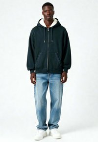 Tume roheline tõmbluku pealeheitega kapuutsiga, millel on valge sherpa vooder, kombineeritud helesiniste lõdva lõikega teksadega ja valgete spordijalatsitega.