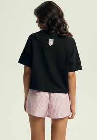 Czarny krótkie t-shirt z logo „COLLEGE 89” w różowym kolorze, w połączeniu z różowymi szortami w kratkę gingham. Miękka tkanina, luźny krój, krótkie rękawy.