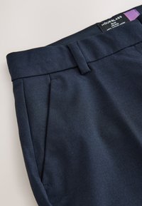 Pantalon bleu marine ajusté avec passants pour ceinture, poche latérale et étiquette de la marque Hourglass visible sur la ceinture.