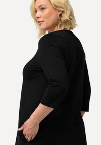 Schwarzes Langarmoberteil mit glatter Textur und lässiger Passform. Mit seitlichen Taschen und Rundhalsausschnitt, mit sichtbaren Nähdetails.