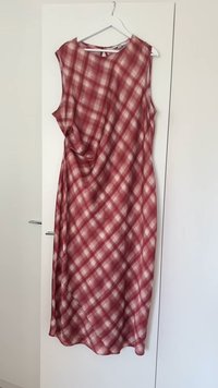 Punainen ja valkoinen ruudullinen midi-mekko ilman hihoja roikkumassa valkoisella hangossa valkoisen vaatekaapin ovessa.