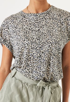 Femme portant un chemisier à manches courtes imprimé léopard, rentré dans un pantalon taille haute vert clair avec un nœud à la taille.