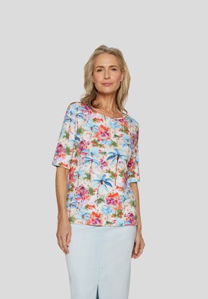 Kurzärmlige Bluse mit floralem Print in Pastellfarben, die auf einem hellen Hintergrund blaue Blumen und Palmen zeigt, kombiniert mit einem hellen Jeansrock.