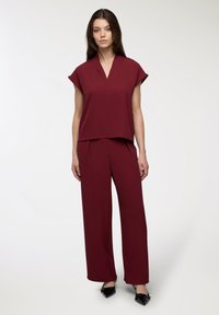 Completo bordeaux in due pezzi, composto da una maglietta a maniche corte con scollatura a V e pantaloni a gamba larga. Tessuto morbido con una vestibilità rilassata e cuciture minime.