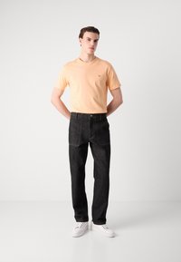 Lettet herres orange bomulds t-shirt, parret med mørke, højtaljede denimbukser med forlommer, afsluttet med hvide sneakers.