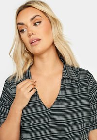 Blusa a rayas en blanco y negro con escote en V, mangas cortas y cuello con botones. Tela ligera con textura suave.