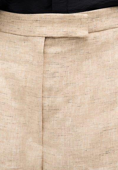 Κοντινό πλάνο μπεζ υφασμάτινου παντελονιού με ύφανση, με κρυφό κούμπωμα άγκιστρο και μπαρέτα στη μέση και κάθετη ραφή στο μπροστινό μέρος.