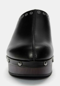 Zwarte leren schoen met een ronde neus, voorzien van metalen studs langs de bovenkant en een gestructureerde houten platformzool. Gladde afwerking.