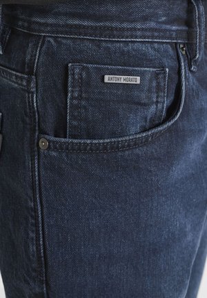 Tamno plava traper jakna s nadstavljenim džepom koji ima crnu oznaku s natpisom "ANTONY MORATO." Tkanina ima suptilnu teksturu i detalje šivanja.