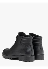 Botas de cuero negro hasta el tobillo con un acabado texturizado, punta redonda y suela acanalada. Incluyen cordones y un cuello acolchado para mayor comodidad.