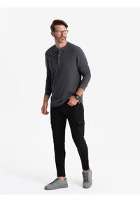 Maglietta henley grigia a maniche lunghe con tre bottoni, abbinata a pantaloni cargo neri e sneakers grigie. Vestibilità moderna con un design informale.