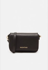 Mala transversal em pele preta da Valentino com letras do logótipo em dourado e alça de ombro ajustável em fundo branco liso.