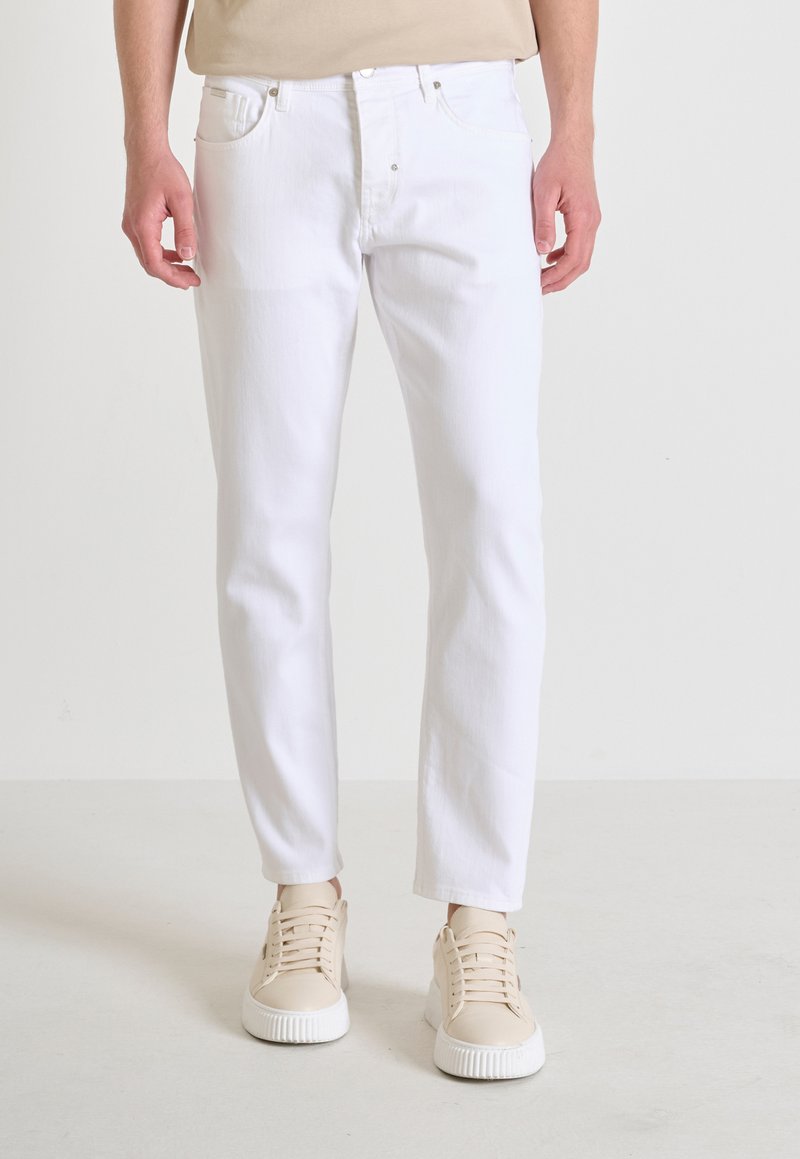 Vaqueros blancos de denim, con un diseño de pierna recta, estilo de cinco bolsillos y costuras claras. Combinados con zapatillas de deporte beige claro.