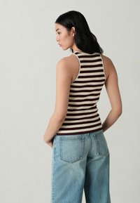 Top a righe in beige e bordeaux, con un design aderente, scollatura rotonda e senza maniche, abbinato a jeans blu chiaro.