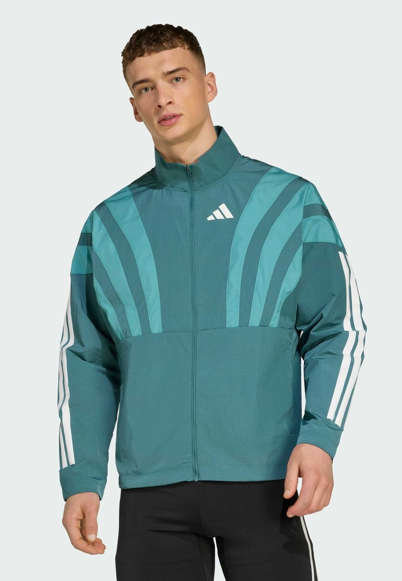 Teal jakna s patentnim zatvaračem sprijeda, visokim ovratnikom i bijelim naglasnim trakama na rukavima. Sadrži grafičke dizajnerske elemente na prsima.