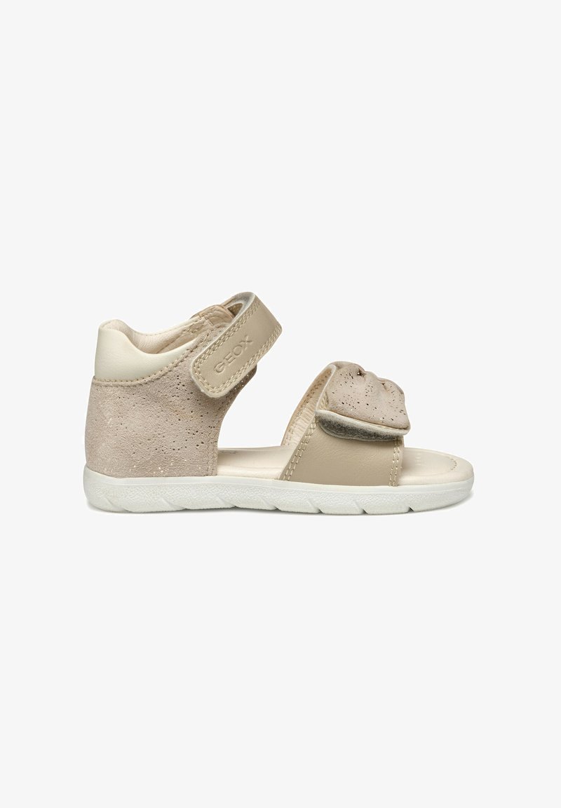 Sandale tan et beige avec une tige en suède texturé, une sangle réglable en Velcro et une semelle en caoutchouc blanc avec un design de semelle flexible.