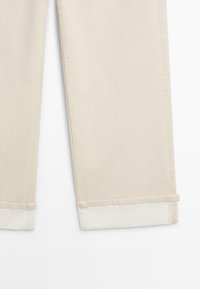 Pantaloni beige con risvolti, taglio a gamba dritta e cuciture visibili lungo le giunture, mostrati su uno sfondo bianco.