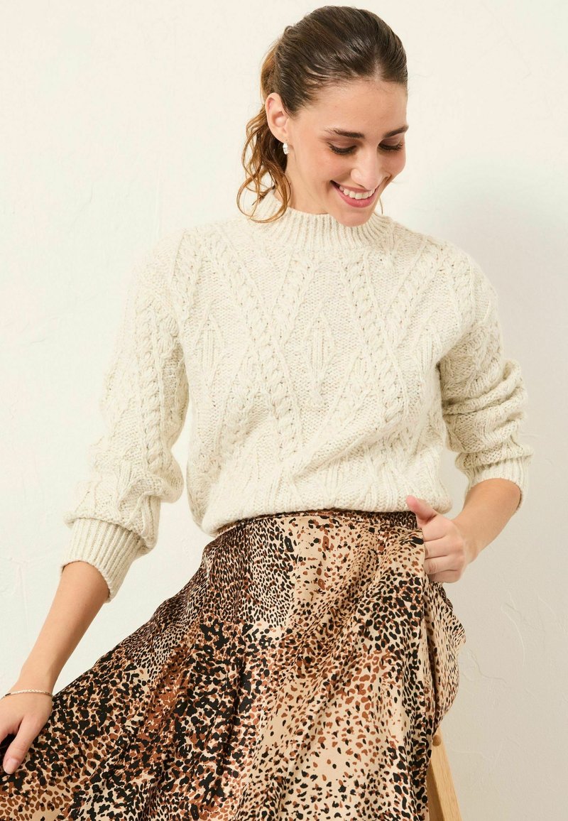 Cremfarbener Strickpullover mit strukturierten Rautenmuster, kombiniert mit einem braun-schwarzen Tierprintrock, der ein fließendes Design aufweist.