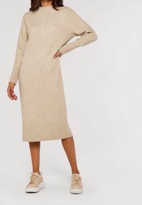 Robe midi beige en maille avec un col rond et des poignets côtelés, associée à des baskets beiges avec des semelles blanches et des lacets.