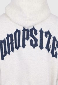 Zadní strana světle šedé mikiny s kapucí, na ramenou je tmavě modrý, třepený gotický nápis "AEROPOSTALE".