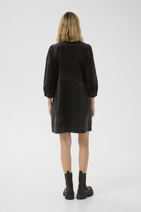Schwarzes Cordkleid mit langen Puffärmeln, knielangem Schnitt und entspannter Passform, kombiniert mit klobigen schwarzen Stiefeletten.