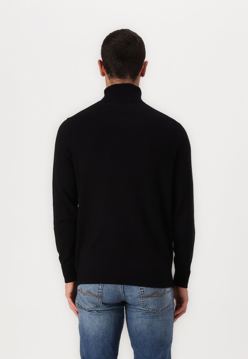 Schwarzer langärmeliger Rollkragenpullover mit glatter Textur und tailliertem Schnitt, kombiniert mit blauen Jeans, die dekorative Nähte an den Taschen aufweisen.