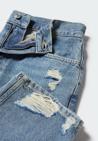 Jean en denim bleu plié avec fermeture éclair partiellement ouverte et détails usés sur les cuisses et les genoux.