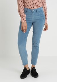 Světle modré kordové kalhoty slim fit, se zapínáním na jeden knoflík a předními kapsami. V kombinaci s černými teniskami.