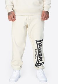 Krämfärgade sweatpants i mjukt tyg, med en svart logotyptryck på sidan. Avslutade med ett elastiskt midjeband och muddar.