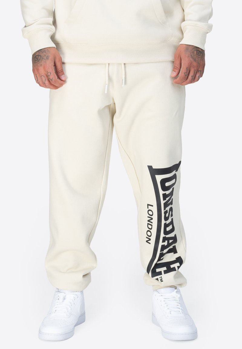 Krämfärgade sweatpants i mjukt tyg, med en svart logotyptryck på sidan. Avslutade med ett elastiskt midjeband och muddar.