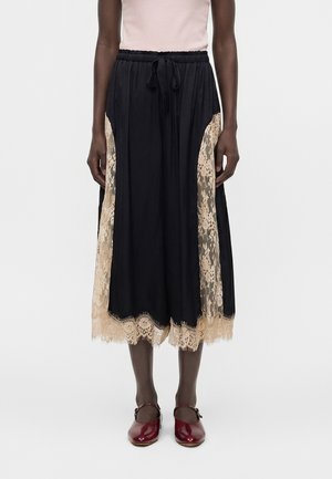 Μαύρη μίντι φούστα με μπεζ δαντελένιες φάσες και τελείωμα, ελαστική μέση με κορδόνι, συνδυασμένη με μπορντό παπούτσια Mary Jane και ανοιχτό ροζ τοπ.