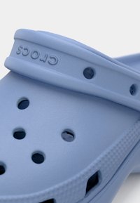 Világoskék Crocs papucsok, melyek texturált felülettel, biztonságos illeszkedést biztosító pánttal és szellőző lyukakkal rendelkeznek. Az anyag sima.