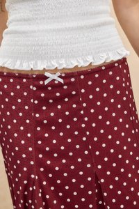 Top alb scurtat cu tiv cu volane, asortat cu o fustă vișinie cu buline albe și o fundiță albă mică în talie.