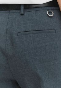 Graue maßgeschneiderte Hose mit glatter Textur, ausgestattet mit einer einzelnen Gesäßtasche und einem metallischen Hardware-Akzent am Bund.
