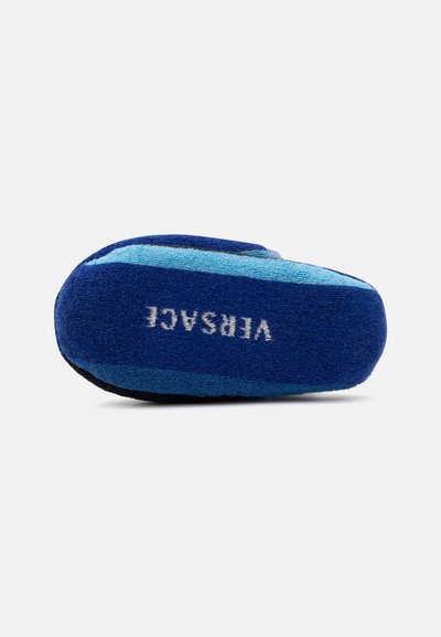 Chausson bleu avec des rayures bleu clair et le mot « VERSACE » brodé en blanc sur la semelle, vu du dessous.