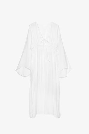 Valkoinen, kevyt mekko V-mallisella kaula-aukolla, kerätyllä vyötäröllä ja laskostetuilla hihoilla. Tekstuuripinta, jossa on solmukohta kaulalla.