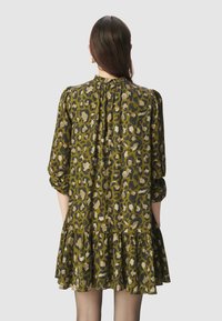 Zielona sukienka w cętkowany wzór z długimi rękawami, marszczonym dekoltem i warstwowym falbanym wykończeniem. Lekki, zwiewny materiał o miękkiej fakturze.