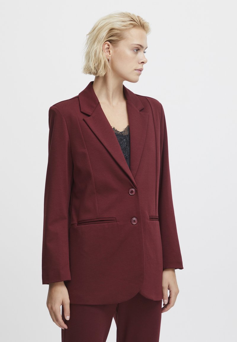 Burgundský blazer z mäkkej tkaniny so štruktúrovaným dizajnom, s klopovými goliermi, dvoma gombíkmi a bočnými vreckami. Viditeľná textúrovaná čierna vnútorná košeľa.