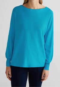 Turkos långärmad topp med bred halsringning, ribbad manschetter och en slät, lätt textur, matchad med mörka byxor.