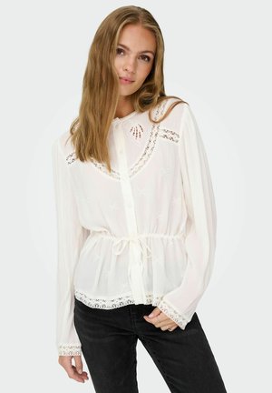 White, button-up blouse with lace trim and floral embroidery. Soft, lightweight fabric with a cinched waist and long sleeves.