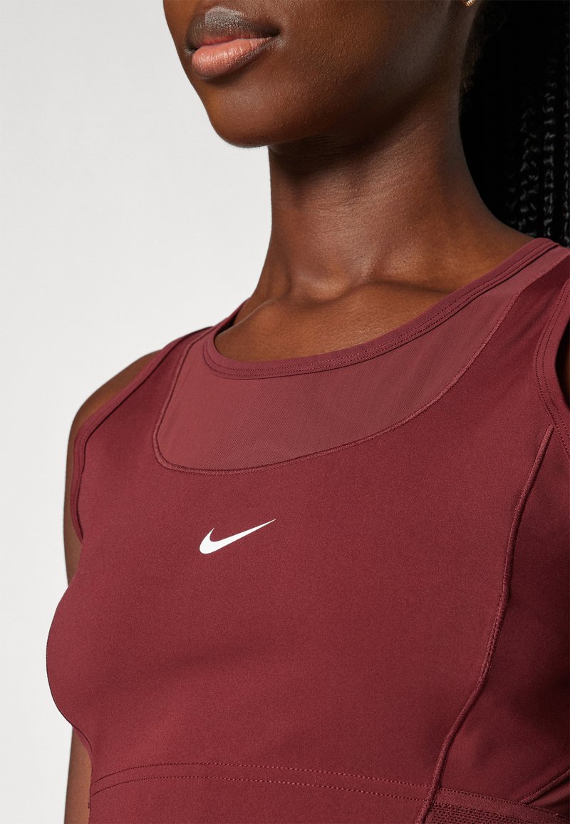 Camisa sin mangas deportiva en color burdeos con un panel de malla, cuello redondo y un pequeño logo de Nike en blanco en el pecho. Tejido suave y elástico.