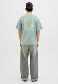 Mintgrøn t-shirt med et botanisk grafiktryk på ryggen. Sammen med løstsiddende, falmede grå jeans og en sort kasket.