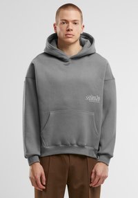 Felpa grigia con cappuccio, dotata di tasca frontale, cordino di regolazione e un logo discreto sul petto. Realizzata in tessuto morbido con una vestibilità comoda.