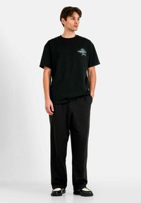 Svart bomullströja med korta ärmar, med en grafisk design på framsidan. Matchas med lösa svarta byxor och svarta skor med vita detaljer.