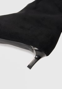 Stivale alla caviglia in suede nero con punta affusolata e tacco alto slim a forma quadrata. L'interno presenta una finitura liscia vicino al tallone.