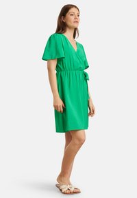 Groene korte jurk met een v-hals, korte mouwen en een strik taille. Gemaakt van een zachte, lichte stof, met een ontspannen silhouet.